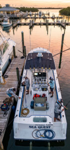 Top-down view of the white fishing boat Sea Quest docked at a marina at sunset, with anglers fishing from the stern.