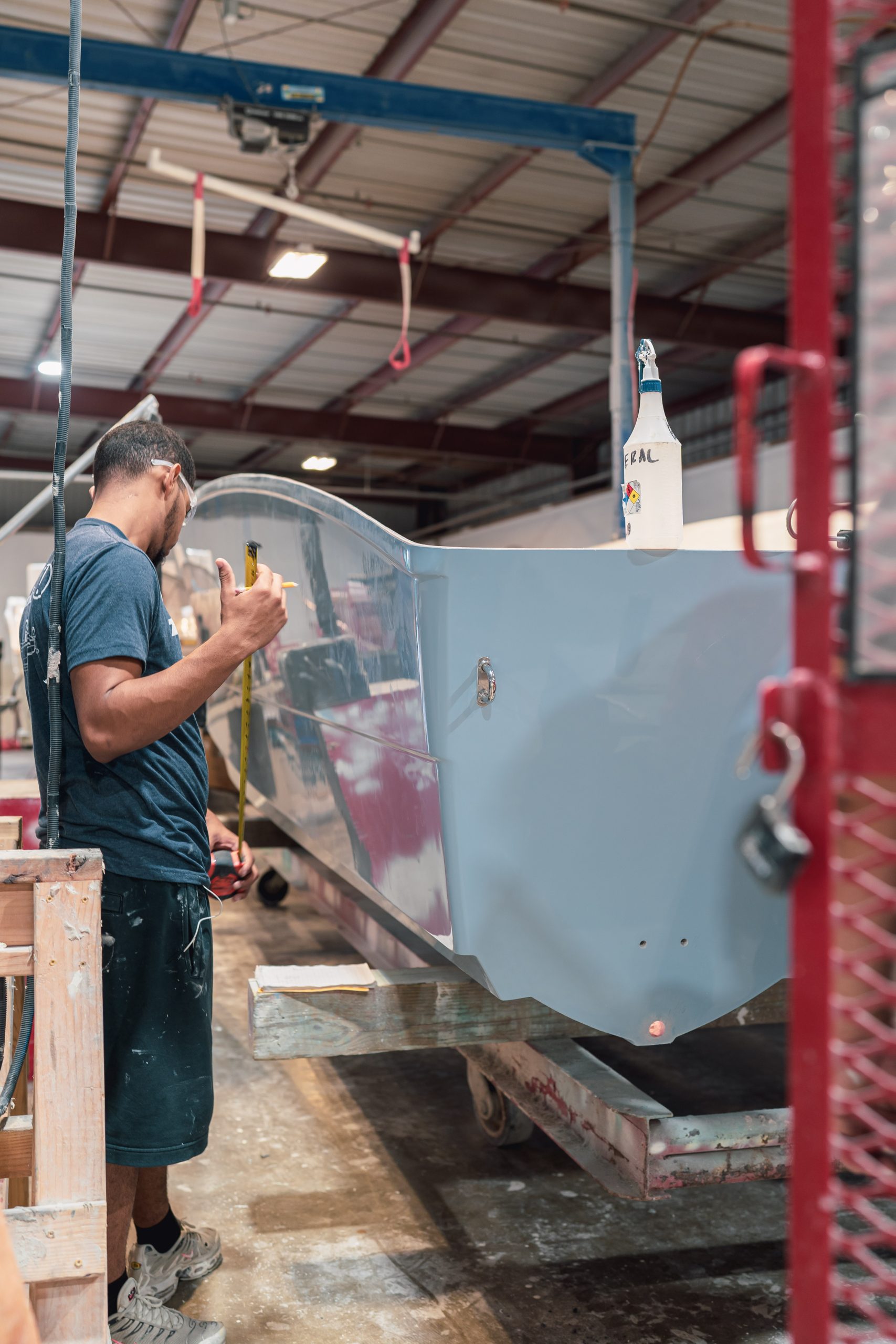 Twin Vee craftsperson measuring alongside a hull during construction at the factory.