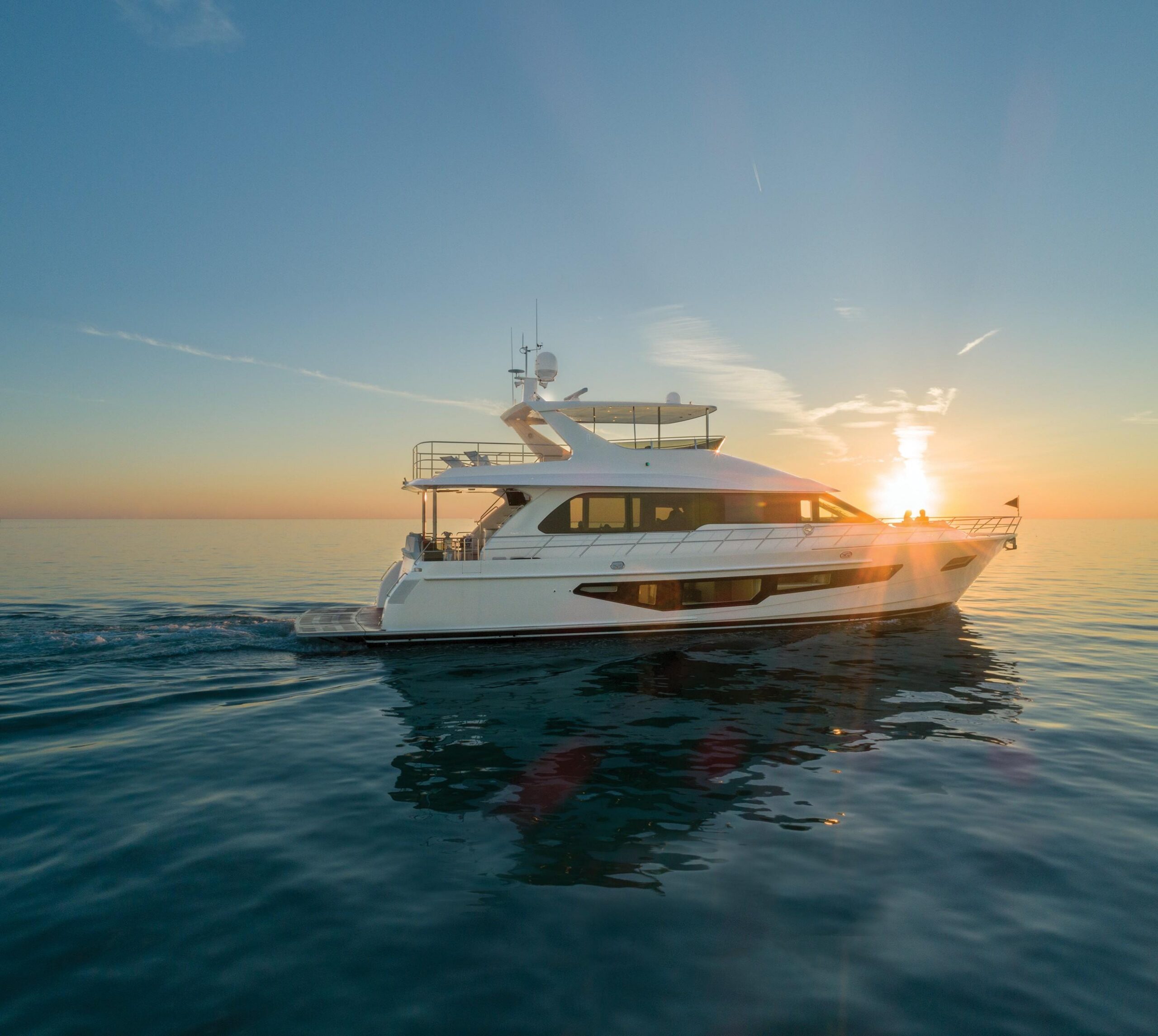 White motor yacht underway on calm water with the low sun beyond its bow.