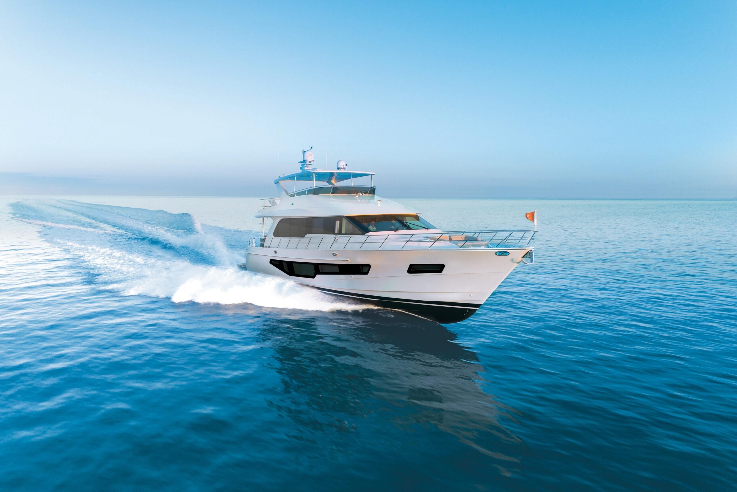 White motor yacht underway on blue water, viewed from the bow quarter with its wake trailing behind.