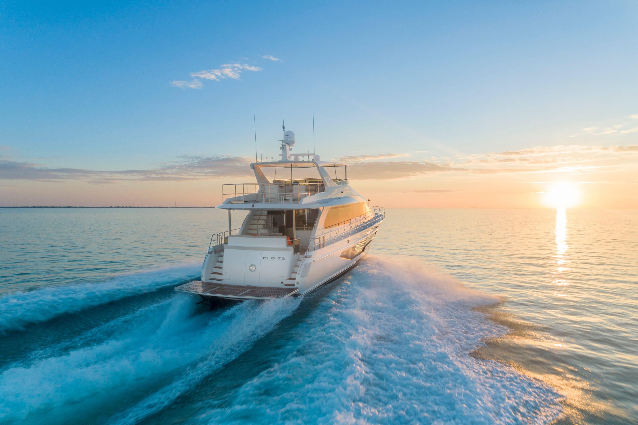 Yacht underway in golden-hour light - Arid Bilge Systems White motor yacht underway across calm water in warm evening light, viewed from the stern quarter.