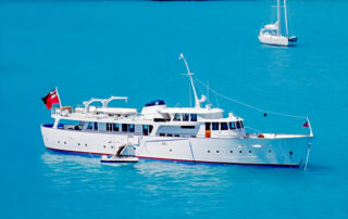 Blue Guitar, the classic white motor yacht, at anchor in turquoise water.