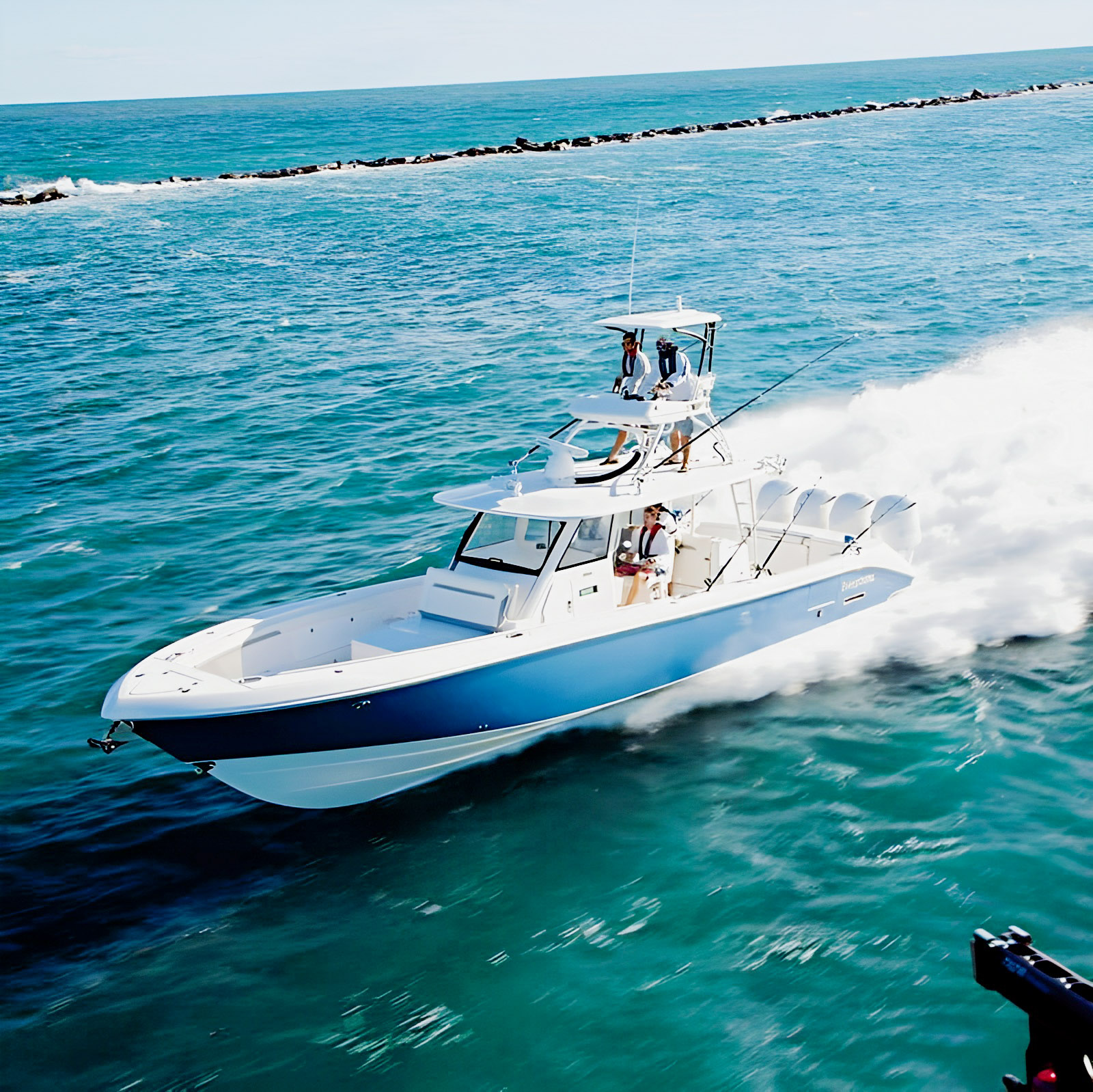 Blue-hulled Everglades center console with four outboards underway near a breakwater.