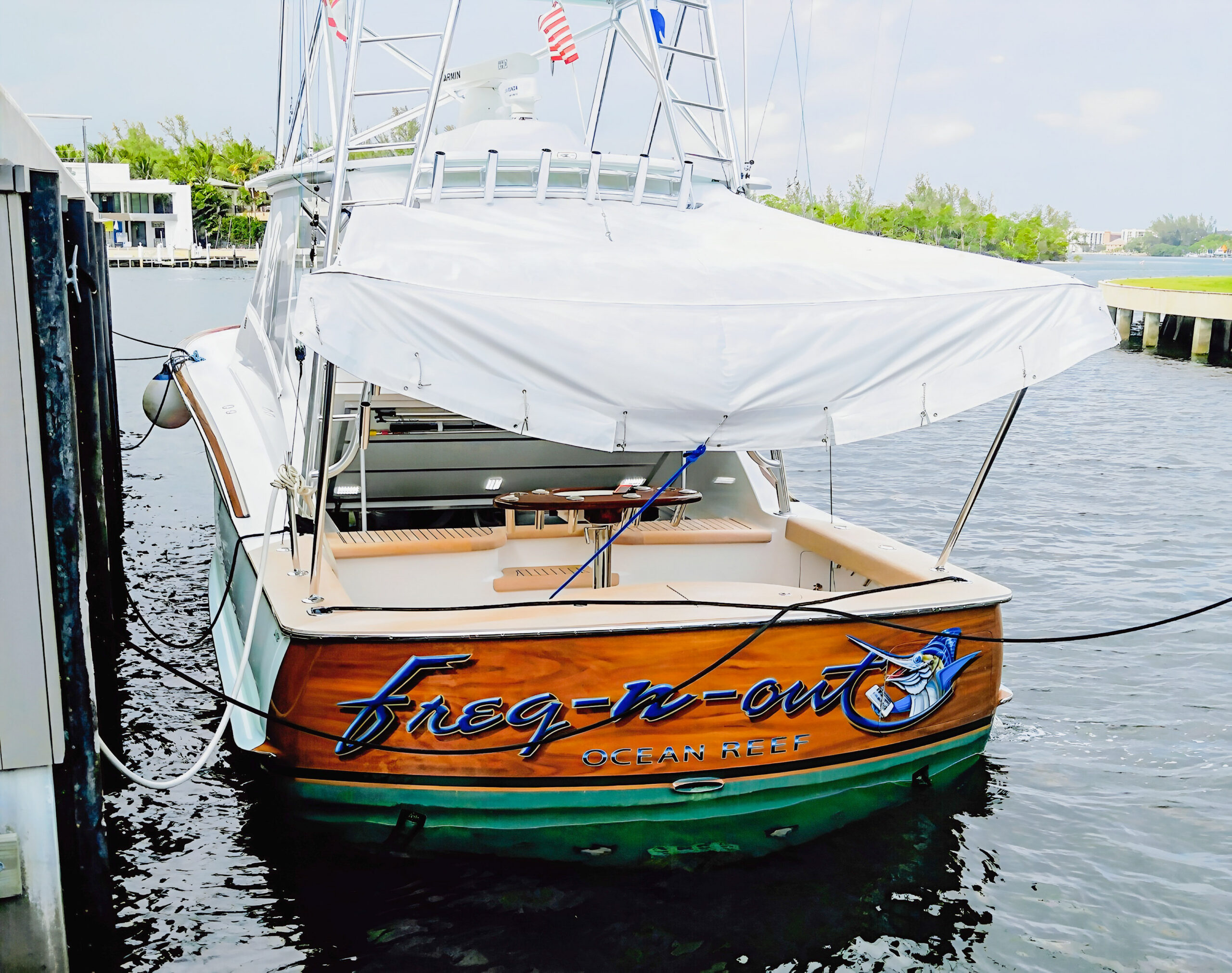 Freq-n-out’s wood-toned transom with blue marlin artwork, its name and Ocean Reef lettering beneath the cockpit shade.