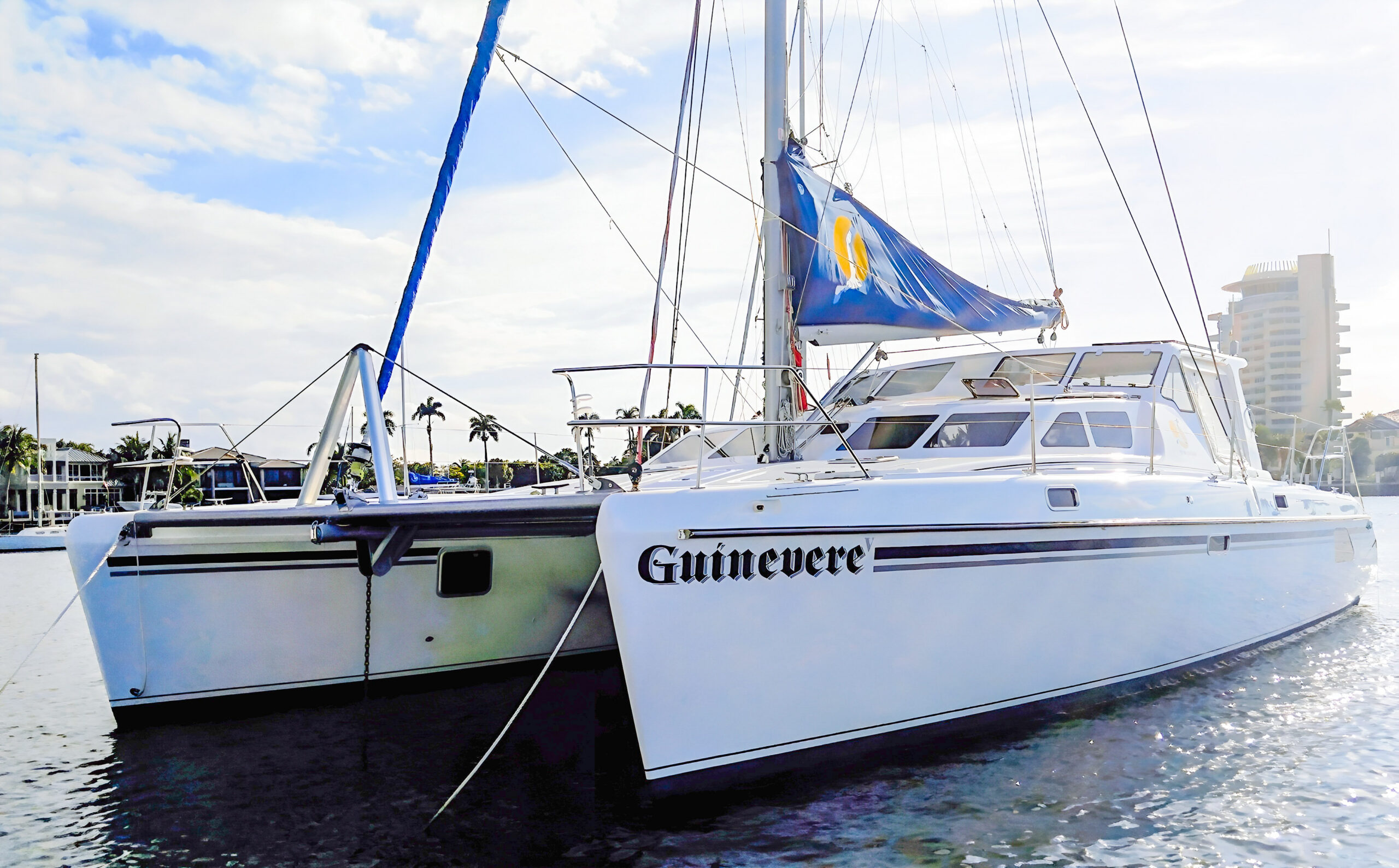 Guinevere V, a white sailing catamaran with twin bows and a blue sail cover, photographed at a dock.