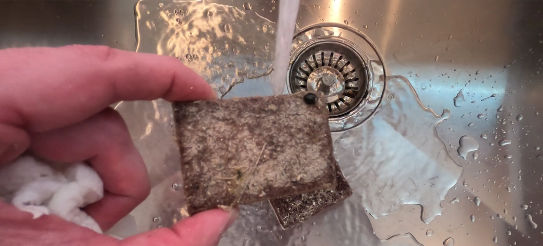 Hand holding a pickup filter pad over a stainless-steel sink during a cleaning demonstration.
